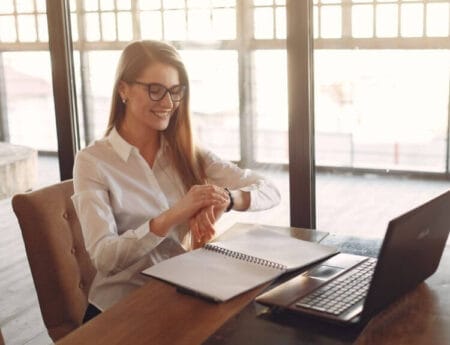 A Person Relaxing in a Tidy Work Space A close-up shot focusing on a person's looking at their watch. They are sitting in a comfortable, clean, and uncluttered office, looking completely at peace. This visual represents the stress reduction benefit.